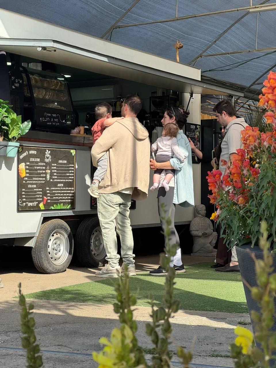 משפחות עומדות ליד עגלת הקפה, ופרחים כתומים בחזית